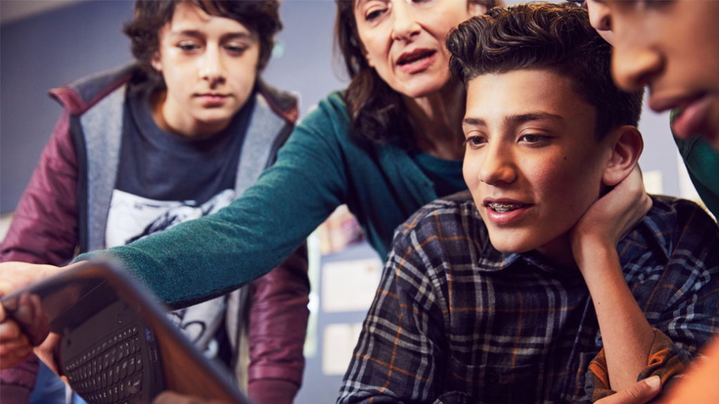 Drei männliche Schüler schauen mit ihrer Lehrerin auf ein digitales Gerät Drei Schüler schauen mit der Lehrerin auf ein digitales Gerät