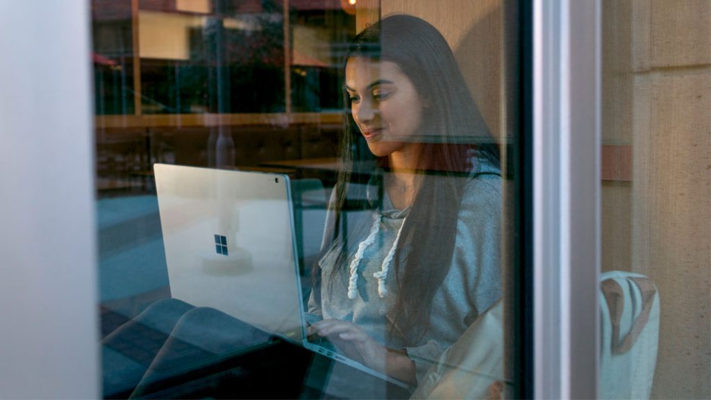 Eine Schülerin sitzt mit einem Surface auf den Boden