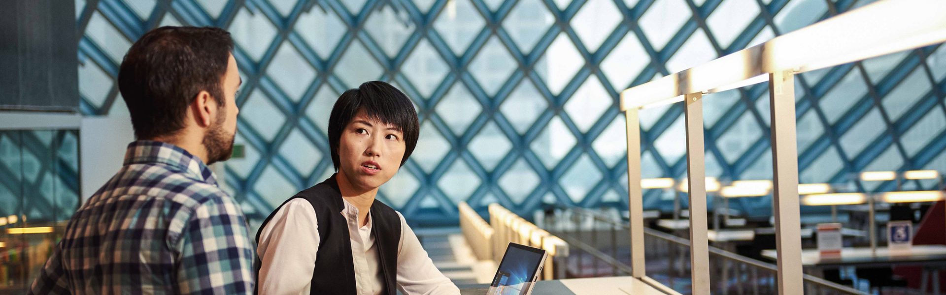 Woman and man sitting at a desk having a conversation in the Seattle Public Library with Surface Pro 4.