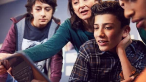 Auf dem Bild sind drei Schüler und eine Lehrerin zu sehen. Alle beobachten einen Computerbildschirm.