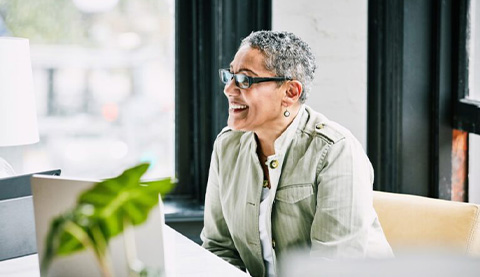 Frau sitzt an Schreibtisch mit Laptop und Pflanze. 