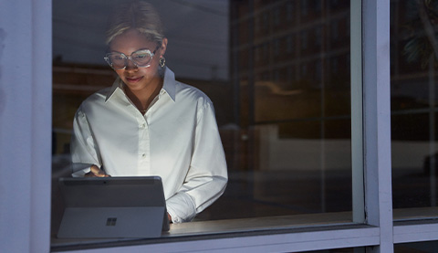 Frau tippt auf Laptop hinter einer Glasscheibe. 