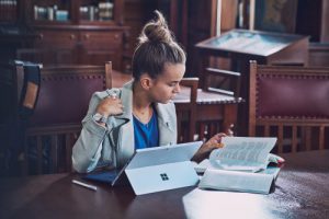 Eine Studentin sitzt in der Bibliothek und lernt mit Büchern und den Microsoft Apps auf dem Surface.