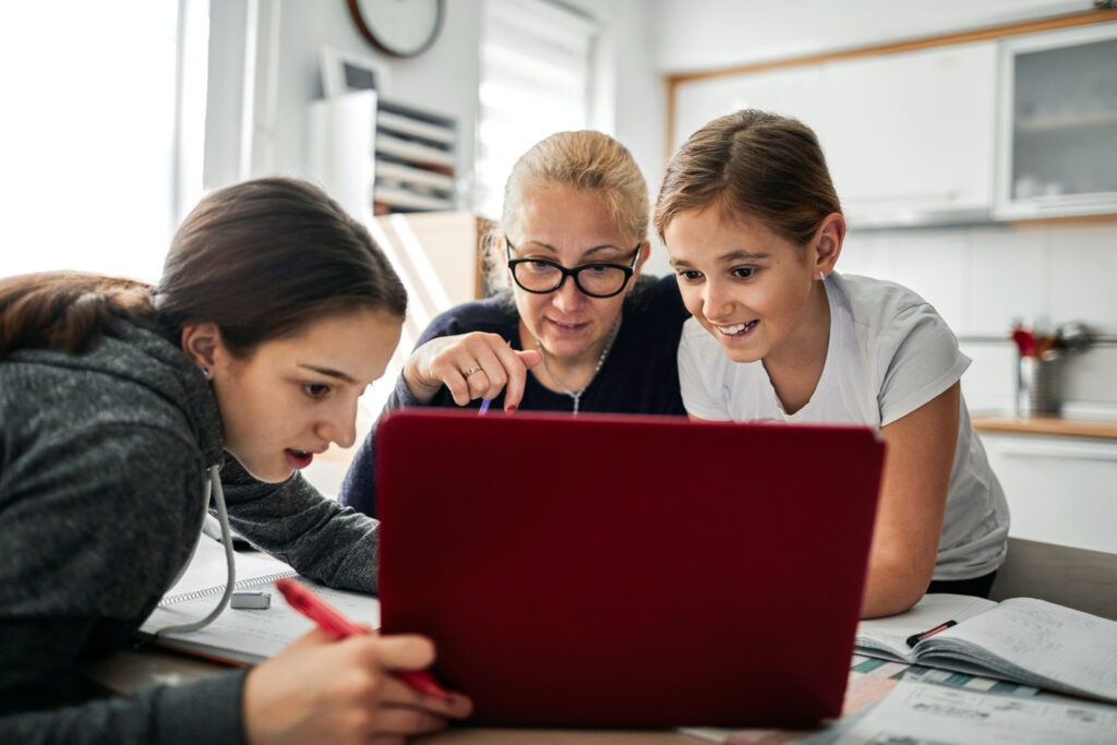 Eine Mutter helft ihren Kindern bei den Hausaufgaben am Laptop.