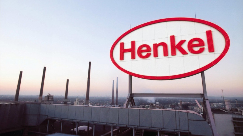 Auf dem Bild ist ein gro&szlig;es Schild vor einer Industriekulisse zu sehen, dass das Henkel Logo zeigt
