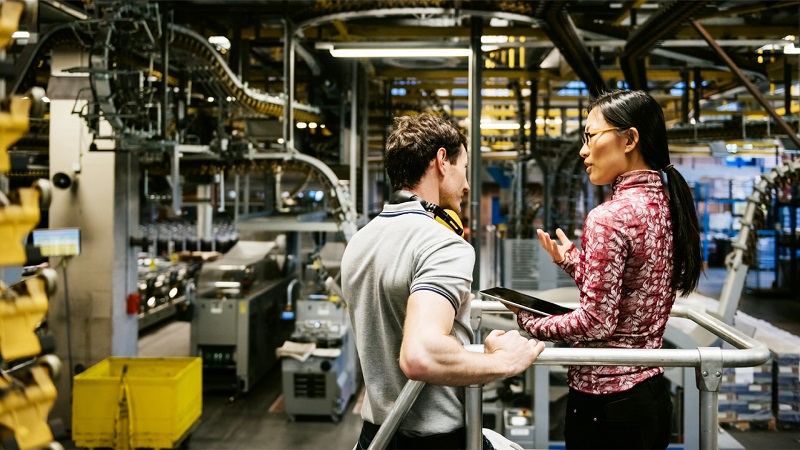 Ein Mann und eine Frau arbeiten an einem Tablet in einer gro&szlig;en Fabrikhalle