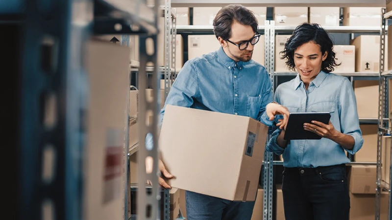 Zwei Personen stehen in einem Lager und bedienen ein Tablet