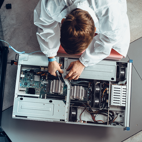Top-down view of a person holding a screwdriver and removing hardware from a server, with exposed wiring and circuitry visible.