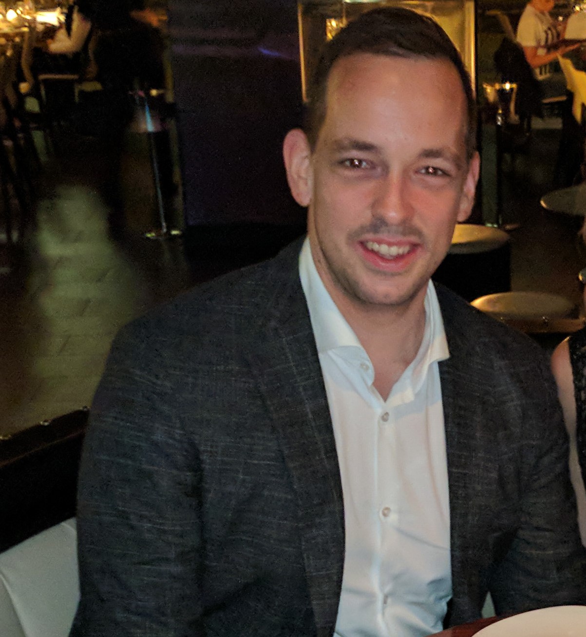 Blair Lochrie, a man with dark hair in a business suit posing for the camera and smiling.