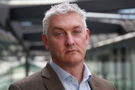 Mark Deighton, a man wearing a suit and tie smiling at the camera