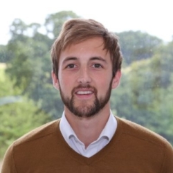 George Tbb, a man smiling for the camera with brown hair and a beard.