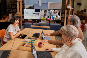 Participants sit at a table looking at a large screen during a Teams meeting.