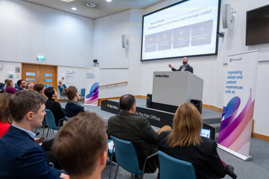 A man standing in front of a podium with a large screen on the wall