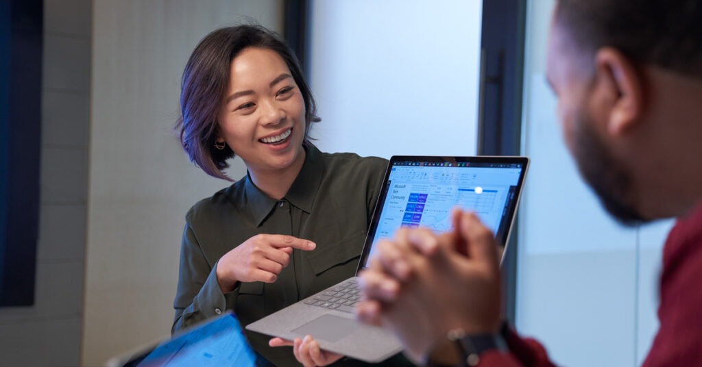 A woman in an office points at her colleague's laptop.