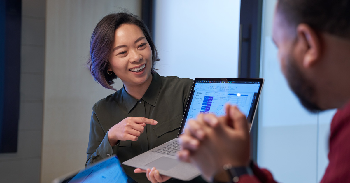 A woman in an office points at her colleagues laptop