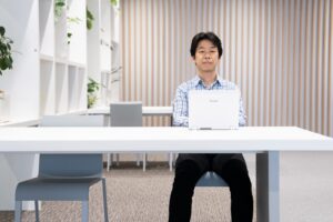 Man sitting behind a desk with a laptop on it, looking straight at the camera