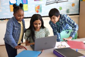 Three students working together on a laptop in a school classroom.