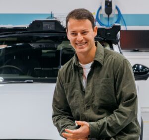 Man wearing coveralls sits on the front of the hood of a self-driving car.