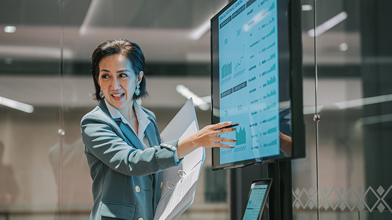 A woman seated at a desk, working on two monitors with a keyboard in front of her.