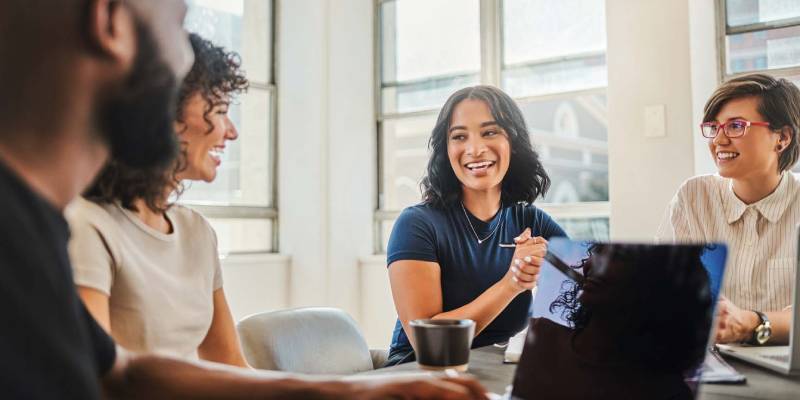 A diverse group of people gathered around a table, collaborating with a laptop in the center.