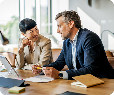Two business professionals seated at a table, collaborating over a laptop during a meeting.