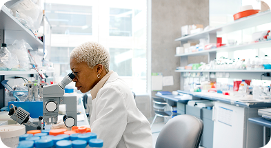 A woman in a lab coat examines a microscope, focused on her research in a laboratory setting.