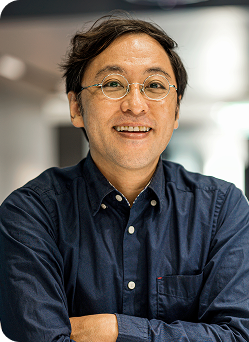 A man wearing a blue shirt stands confidently, showcasing a casual yet polished appearance.