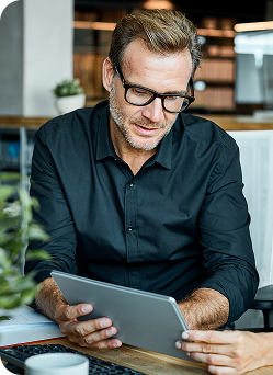 A man at a desk, discussing documents and using a laptop, with a focused expression.