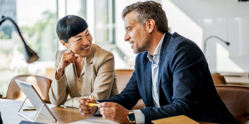 A man and woman in business attire are collaborating while looking at a tablet together.
