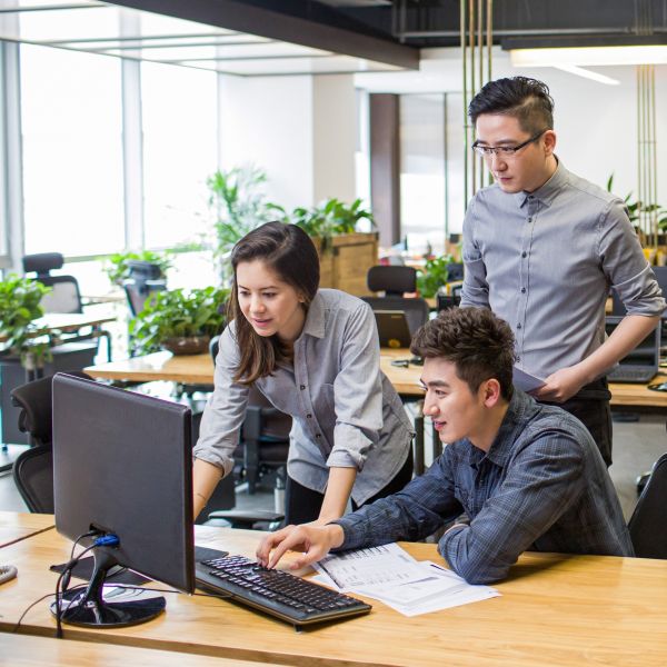 IT professionals gather around a computer in a modern open office space.