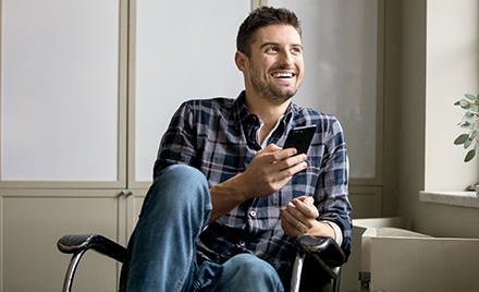A man sits back in his chair, smiling and holding a smartphone