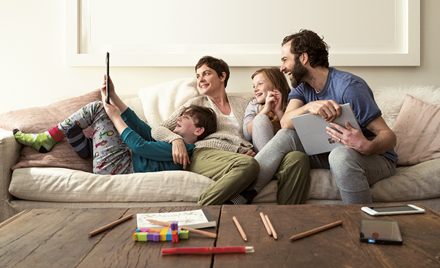 A family sits on a couch holding smart devices and laughing