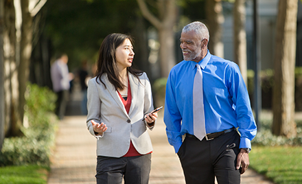 Image of two employees walking along a sidewalk discussing something over a mobile device