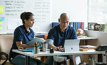 Image of two firstline workers sitting behind a desk making plans on their laptops