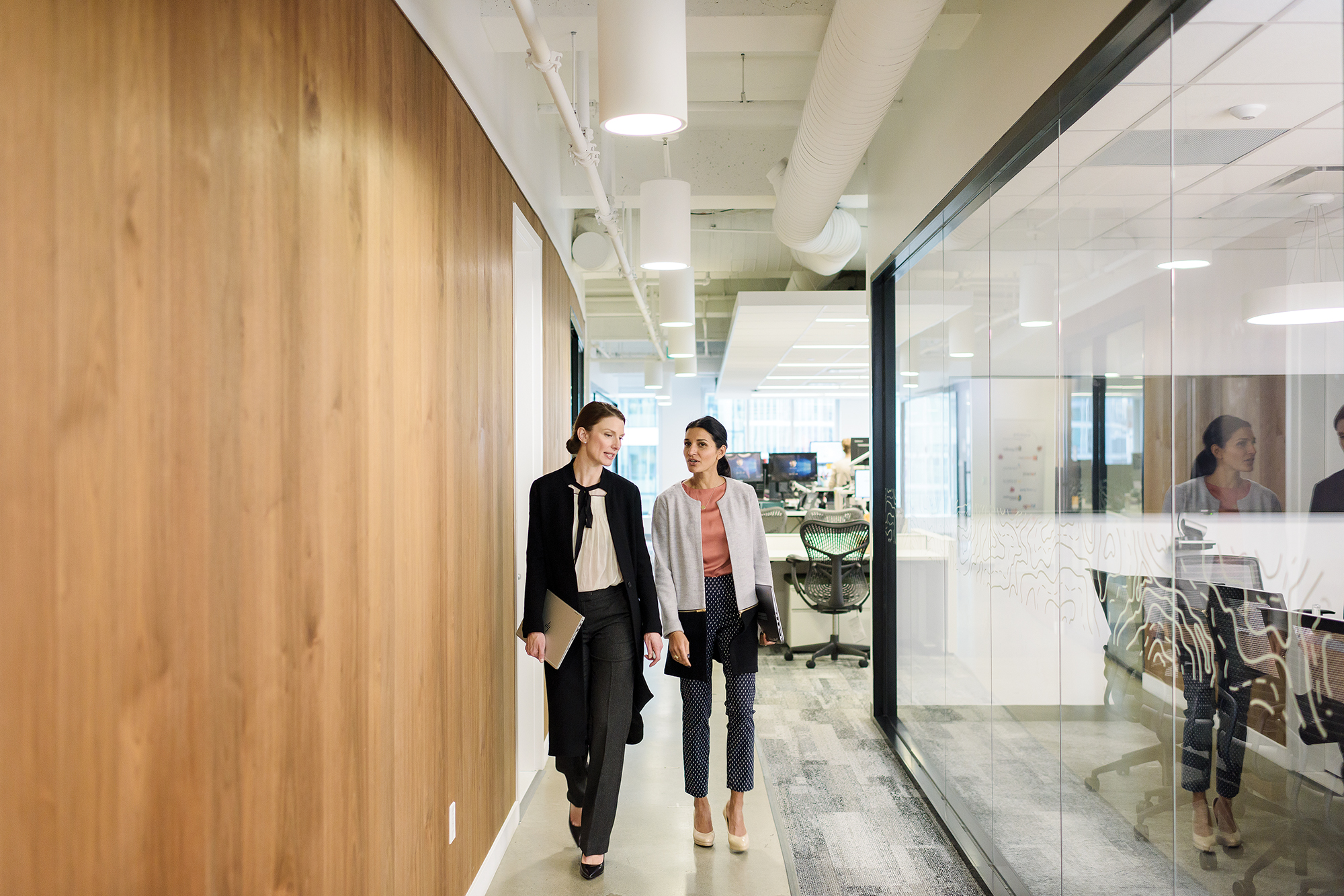 Two workers chat and walk down a hallway