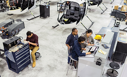 Image of workers assembling a helicopter. Several are gathered around a laptop