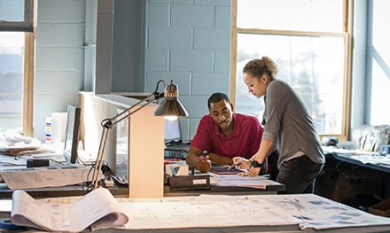 Two coworkers collaborate over a document on a desk