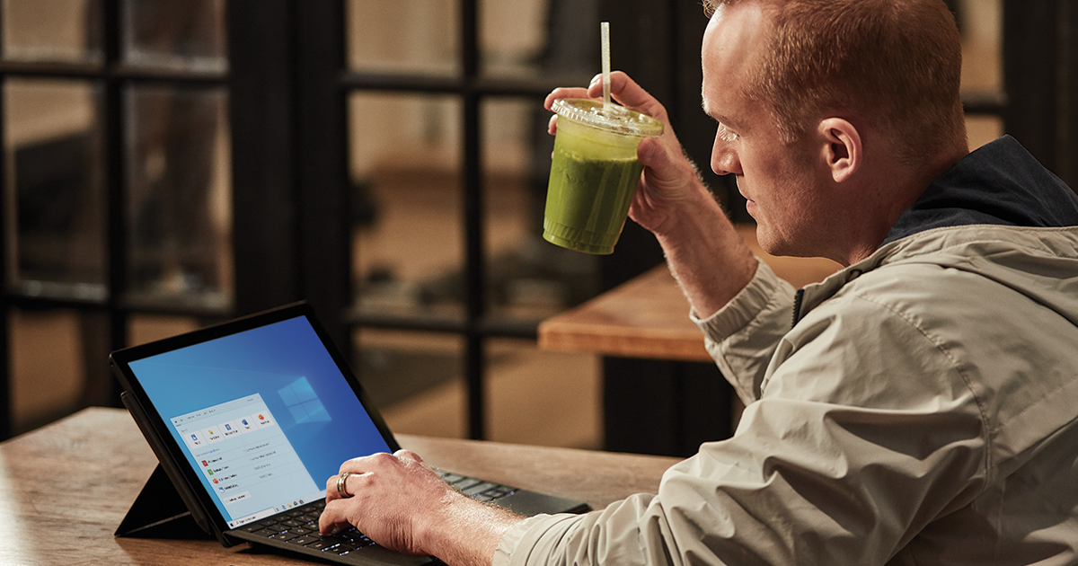 An IT worker holding a smoothie and working on his laptop