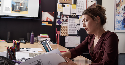 An image of a female small business professional working on designs using devices running PowerPoint and Microsoft Teams