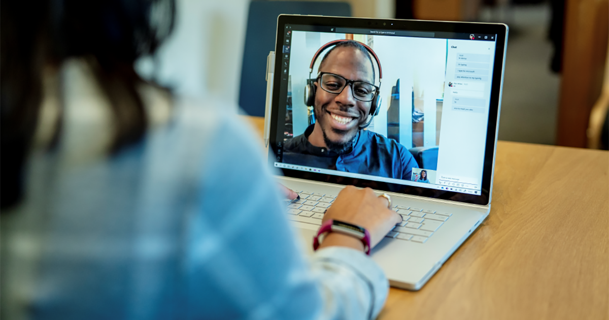 Image of a woman at a desk using a Surface laptop to make a Microsoft Teams video call with one man smiling and wearing a headset