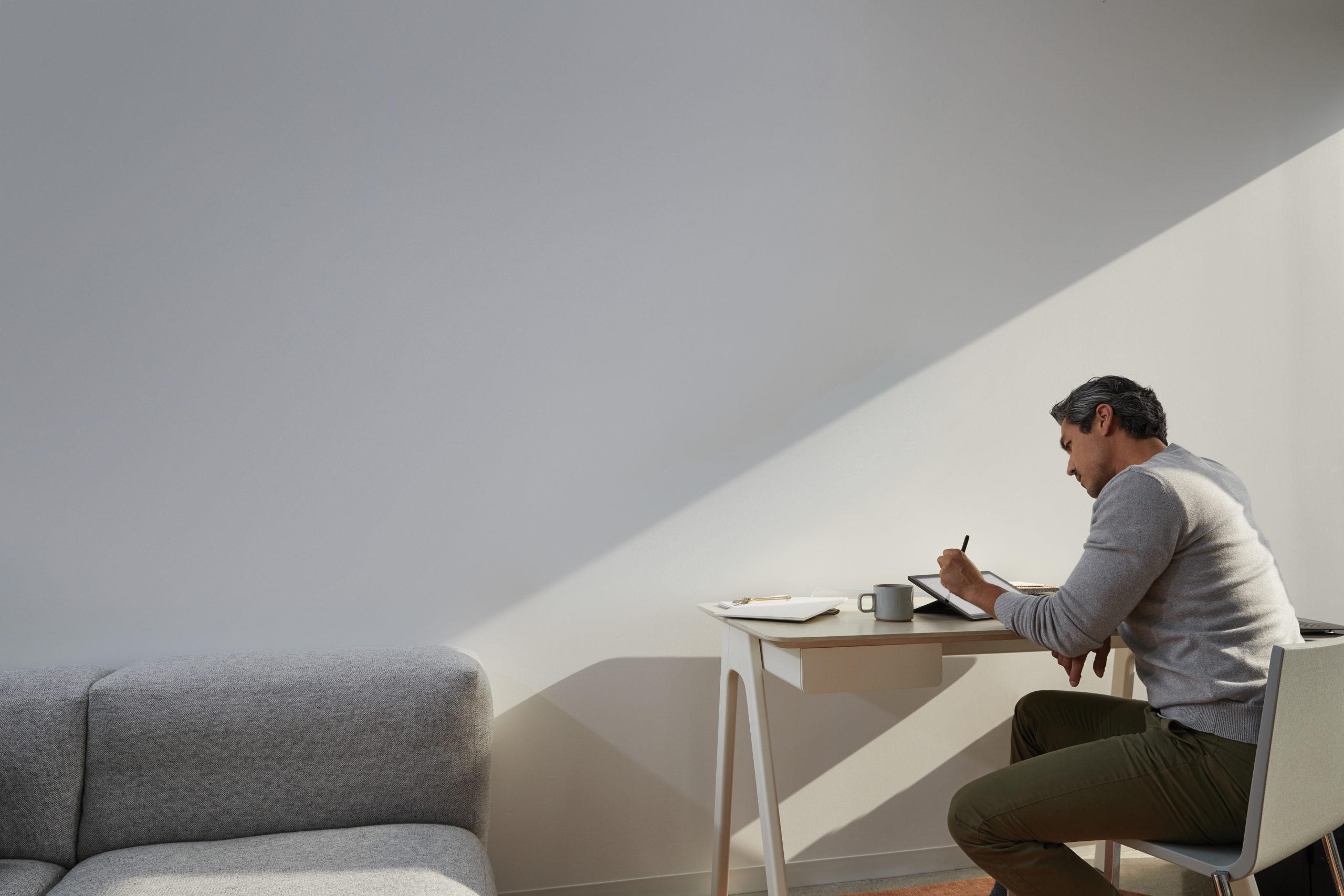 Adult male in home office environment sitting at a desk with a black Microsoft Surface Pro 7 in studio mode. Black Microsoft Surface Pen in hand
