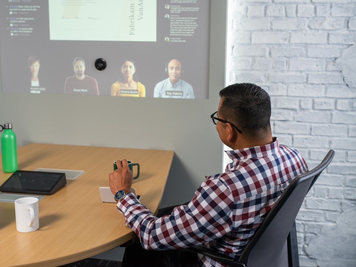 Adult male sitting at conference table looking at screen projected on wall