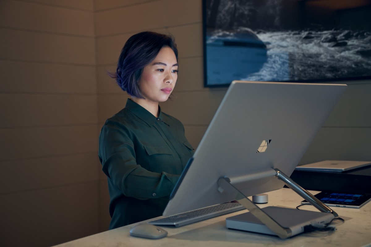 Side profile of a woman wearing a dark shirt in a dim office working on a Microsoft Surface Studio