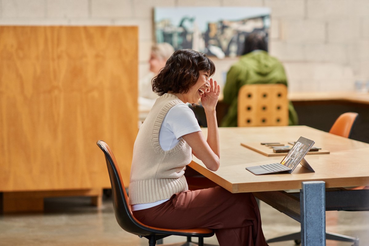A woman participating in a Microsoft Teams meeting on a Surface device while hotdesking in an open work space​
