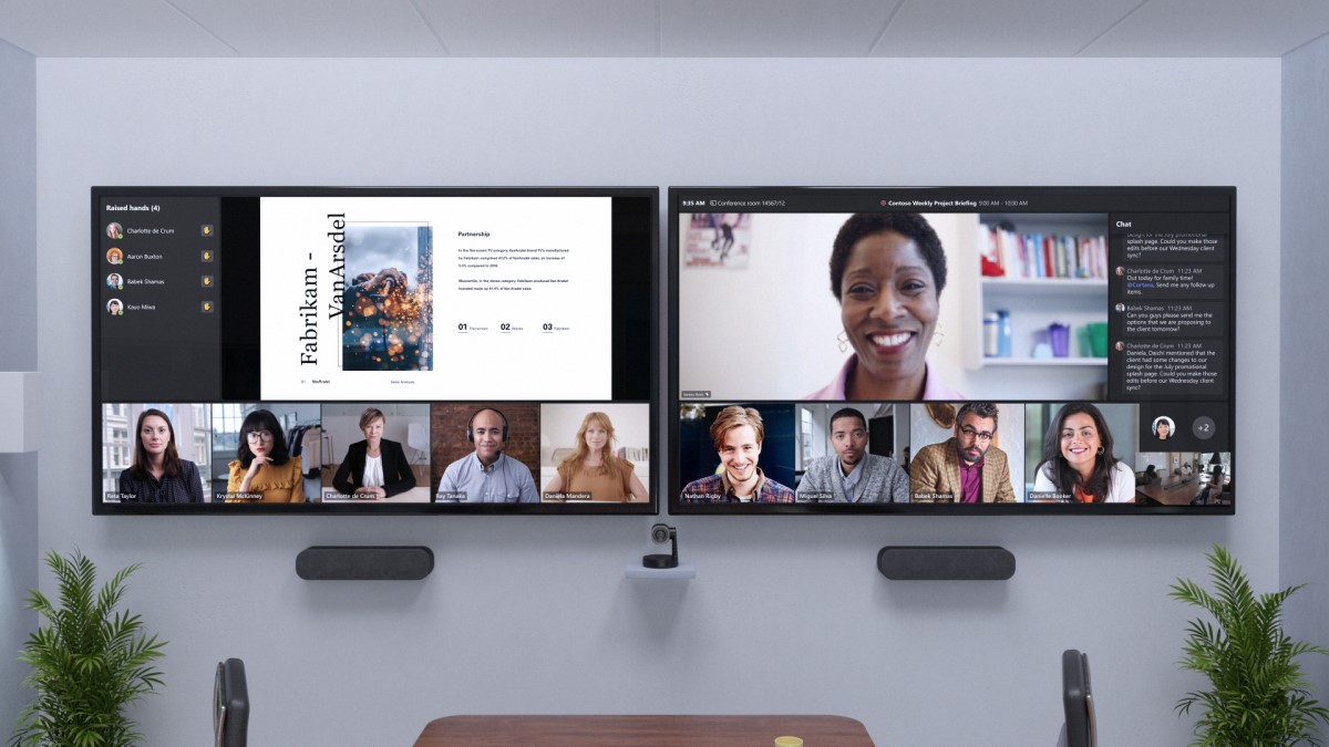 Remote attendees are across two front of room screens at eye level beside chat and a view of participants with raised hands.