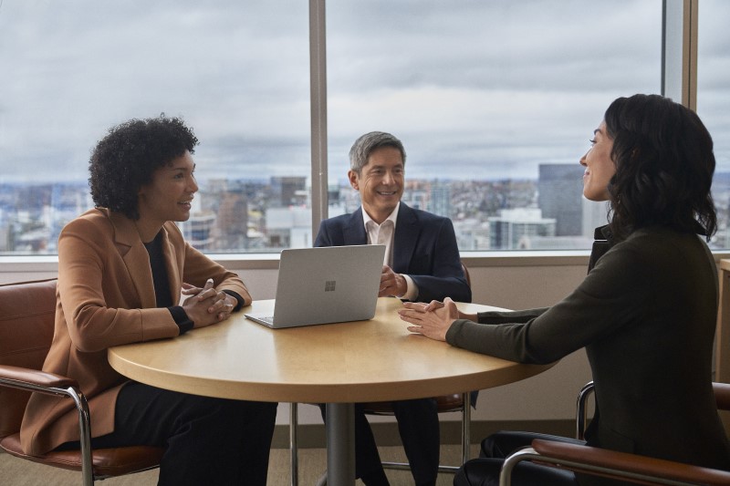Three people meeting at a conference table with a Surface Laptop Go 2