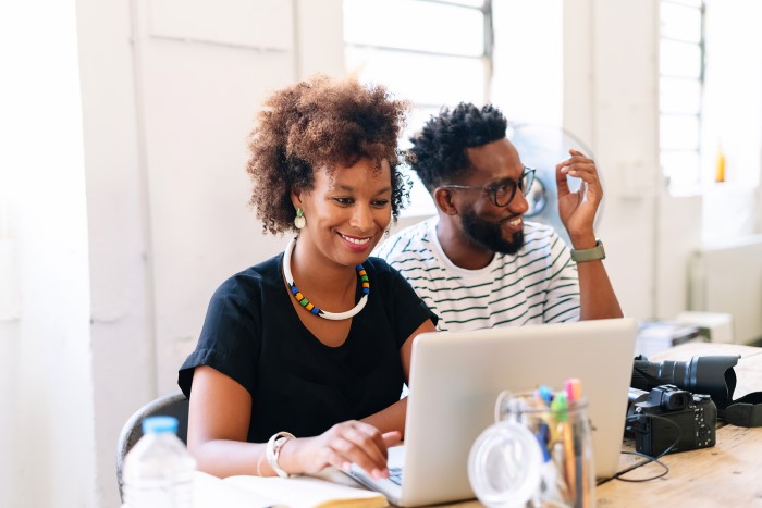 Two graphic designers sit in front of an open laptop