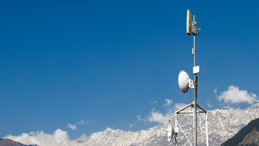 Communication tower with dishes under clear blue sky, snowy mountains in background.