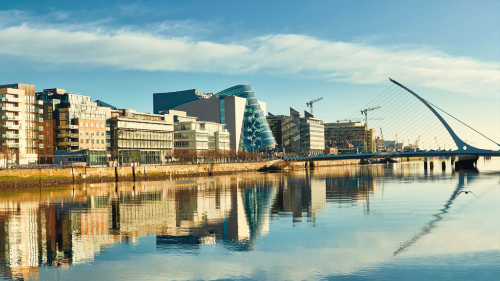 Modern buildings and the Samuel Beckett Bridge reflect on the River Liffey under a blue sky.