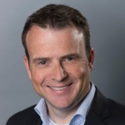 a man wearing a suit and tie smiling at the camera